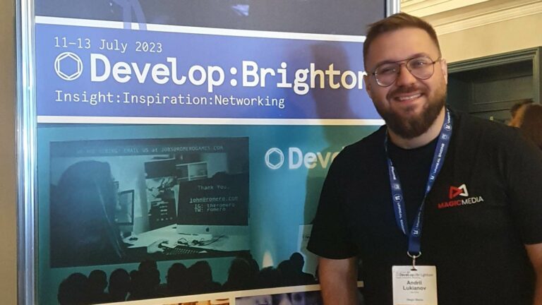 Magic Media team member at the Develop:Brighton event, smiling and standing in front of a promotional banner.